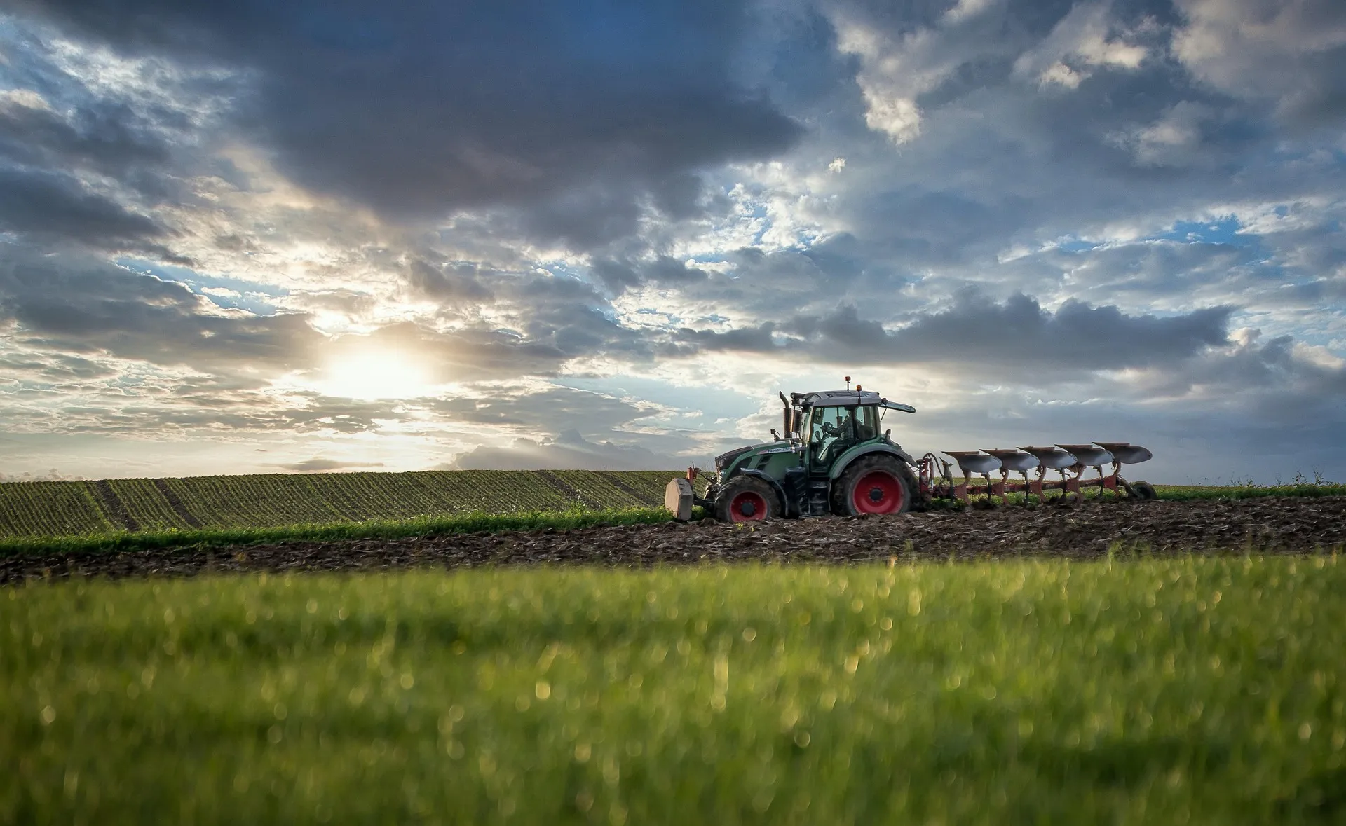 Tractor pulling a plow across a field at sunset under a cloudy sky