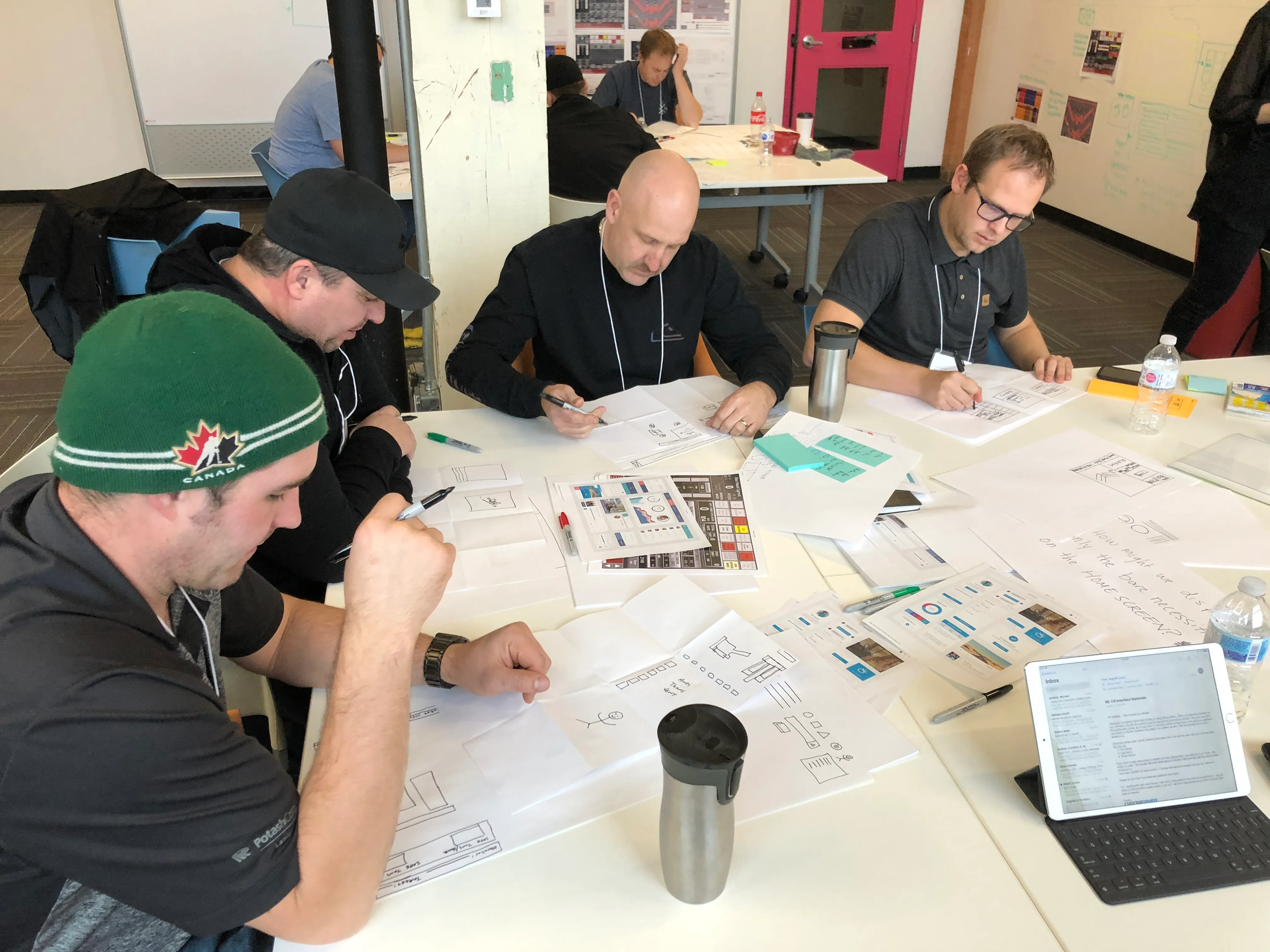 Panoramic workshop session with two presenters and sticky-note mapping on the wall