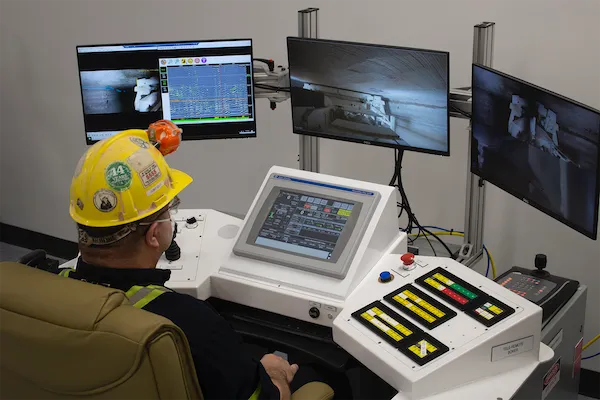 Miner operating a tele-remote control console with multiple camera and data monitors