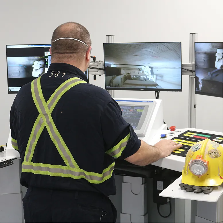 Rear view of an operator at a mining control station with a hard hat on the side table