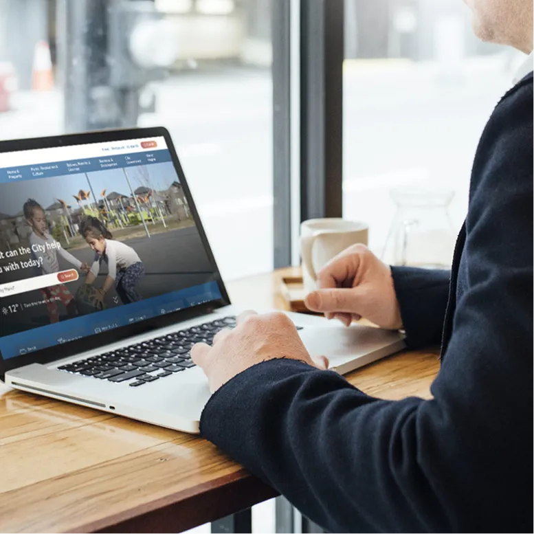 Person using a laptop displaying the City of Regina website at a table
