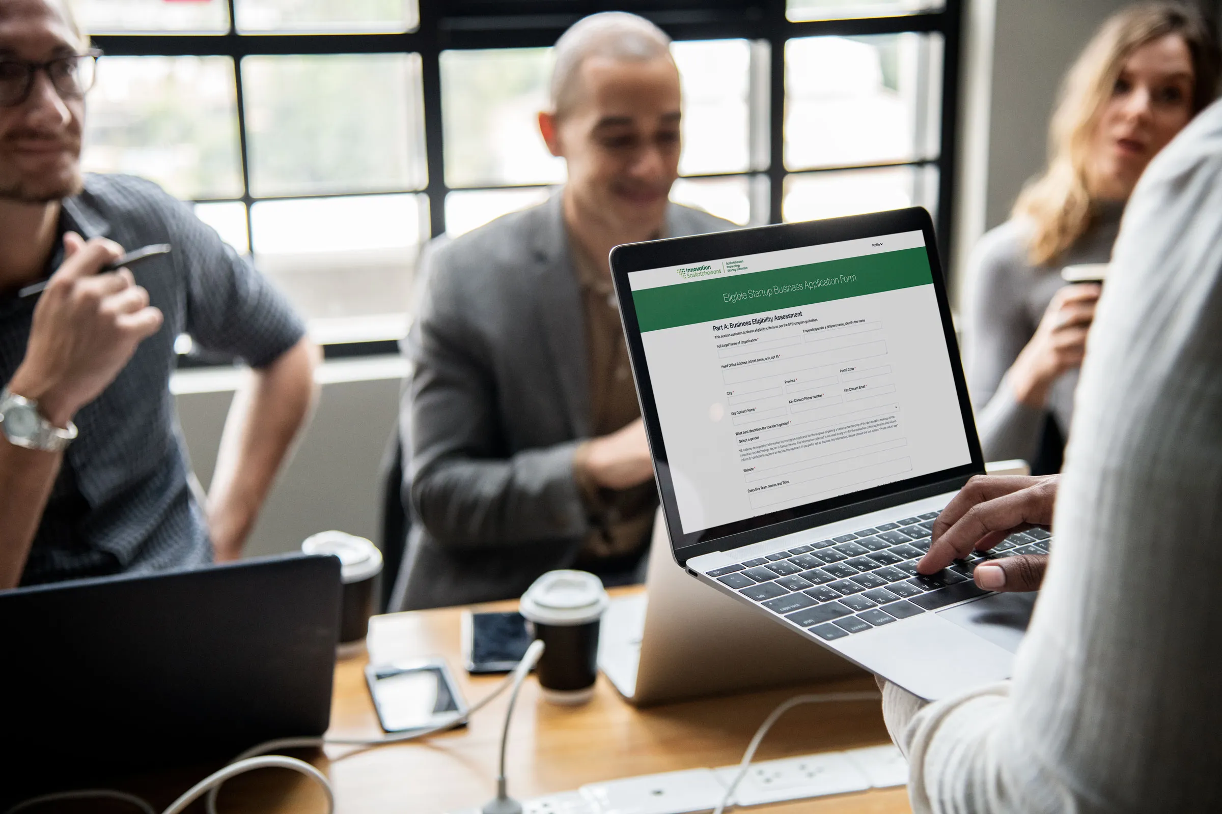 Team meeting scene with a laptop in the foreground displaying the Eligible Startup Business Application form