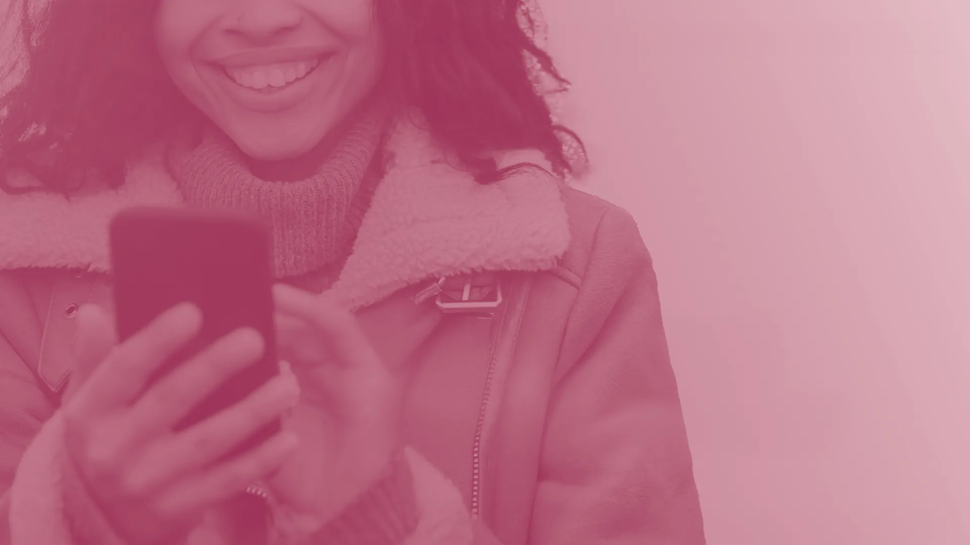 Smiling person in a coat using a smartphone, with a pink overlay.